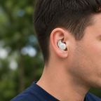 Alpine White Tuck Bud worn in a man's ear outdoors, with blurred green trees behind him
