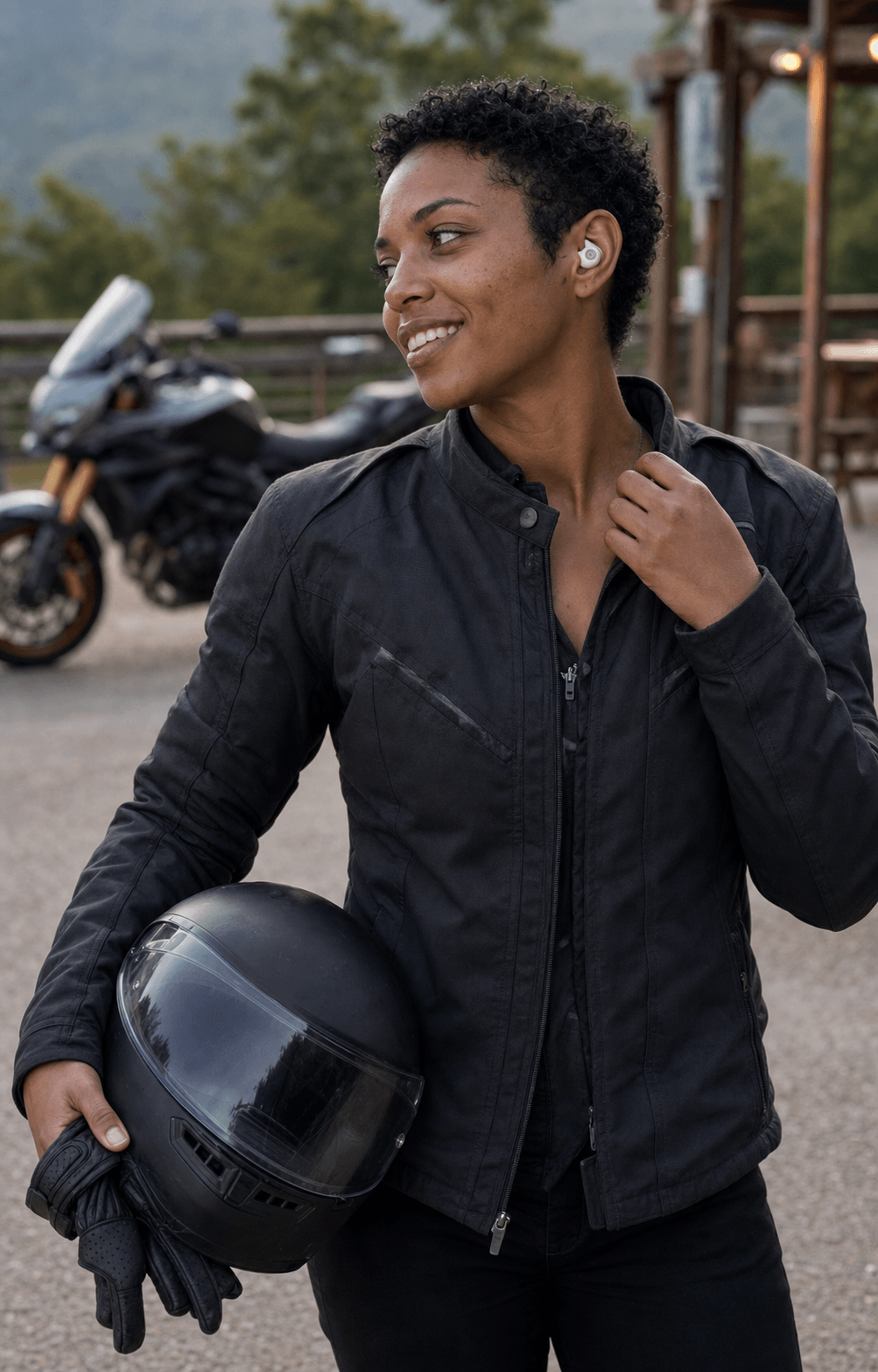 Rider wearing an Alpine White Tuck Bud, holding her helmet and gloves beside her motorcycle